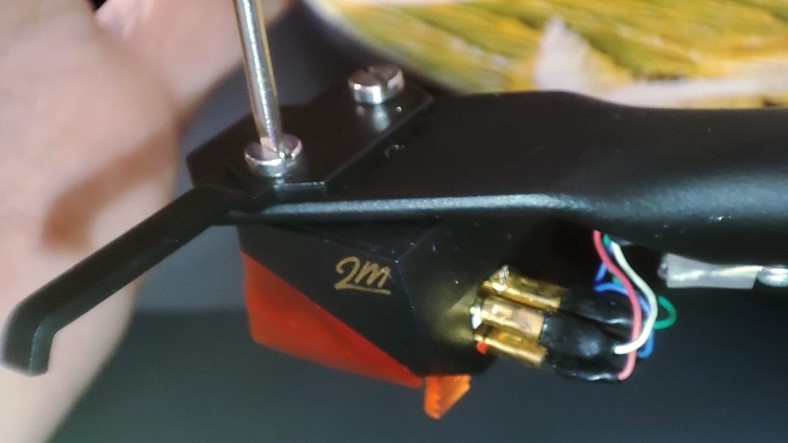 Close-up of a tonearm headshell showing the four coloured cartridge wires and mounting slots for cartridge fitting